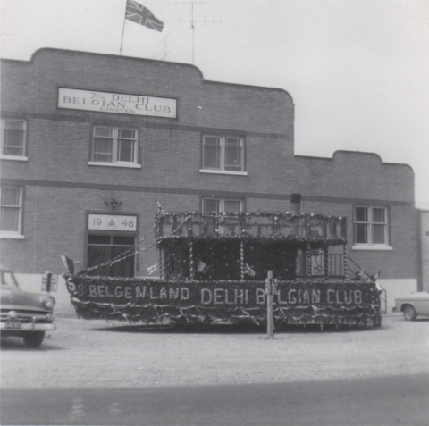 B/W photo of a parade float in front of the Delhi Belgian Club decorated with "S.S. BELGENLAND DELHI BELGIAN CLUB" along with Belgian and union jack flags